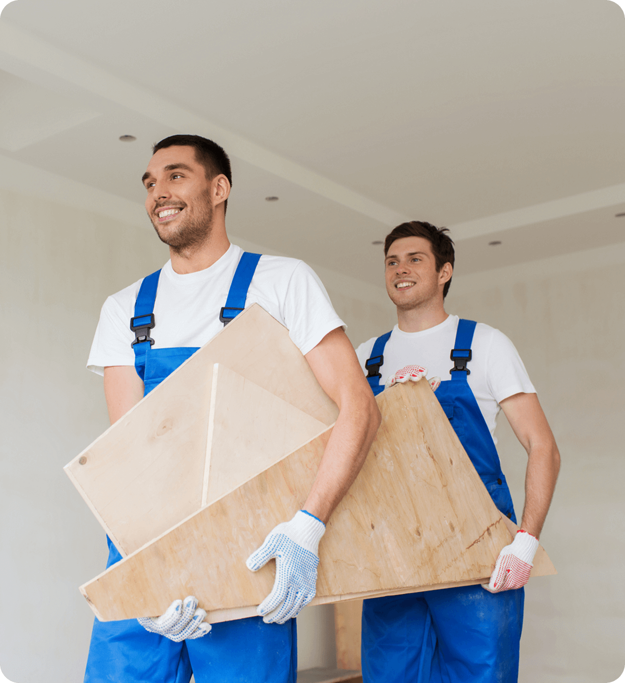 Construction workers carrying wooden boards indoors.